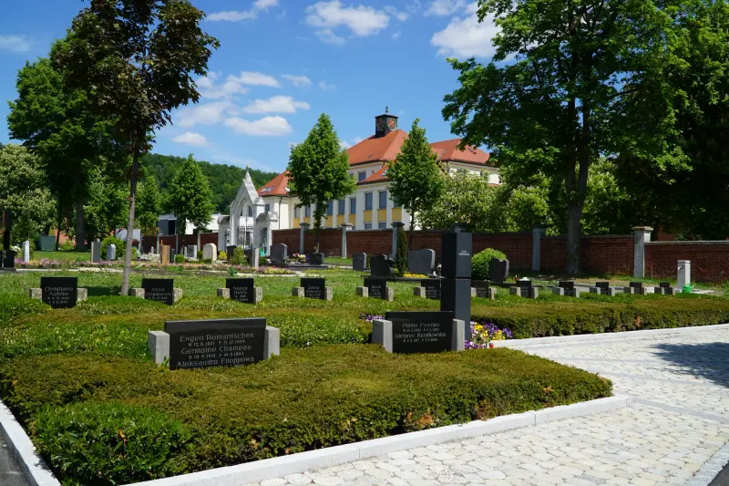 Kwatera z. nagrobkami na Totenbergfriedhof w. Heidenheim an der Brenz, w. tle brama i. budynek z. czerwoną dachówką — Powiat Heidenheim